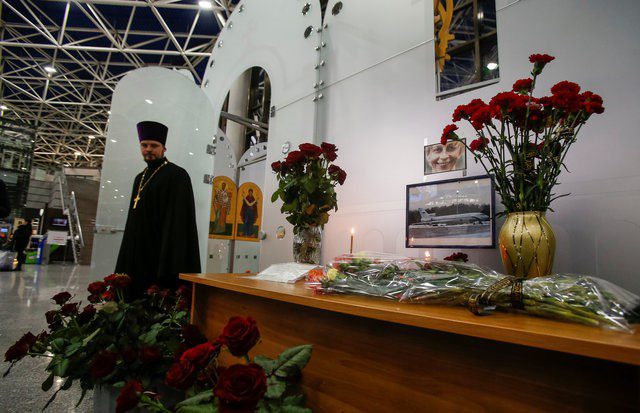 A priest looks at flowers placed in front of pictures of Tu-154 plane and head of 'Fair Aid' fund Elizaveta Glinka, to commemorate passengers and crew members of Russian military plane, which crashed into the Black Sea on its way to Syria on Sunday, at the Sochi International Airport (Sochi-Adler Airport) in the Black Sea resort city of Sochi, Russia, December 26, 2016.  REUTERS/Maxim Shemetov